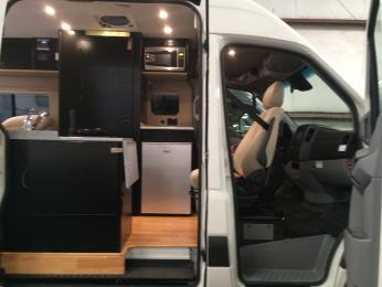 Lonwood flooring and black cabinets with tundra countertops, tan trim, and Isotherm elegance fridge.  Small microwave above counter behind driver's seat.
